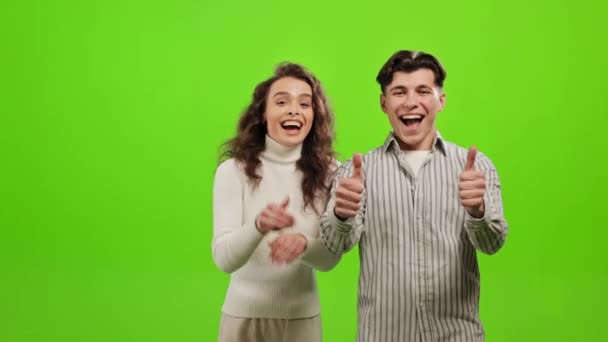 한 남자와 한 여자가서 서 카메라를 보고 있습니다. 그 들은 손가락을 위로 치켜들고 미소를 짓습니다. 그 들은 푸른 배경 위에 서 있습니다. 녹색 화면. 4K — 비디오