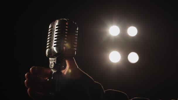 Il cantante sta prendendo un microfono retrò con la mano. I riflettori puntano su di lui. Sparatoria ravvicinata. 4K — Video Stock