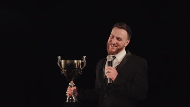 Un uomo è in piedi sul palco e parla. Ha in mano la coppa dei vincitori e il microfono. I riflettori puntano su di lui. 4K — Video Stock