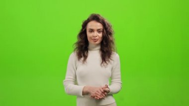 Kadın ayakta duruyor ve kameraya bakıyor. Ellerini birarada tutuyor ve gülümsüyor. O, yeşil bir arka planın üzerinde duruyor. Yeşil ekran. 4K