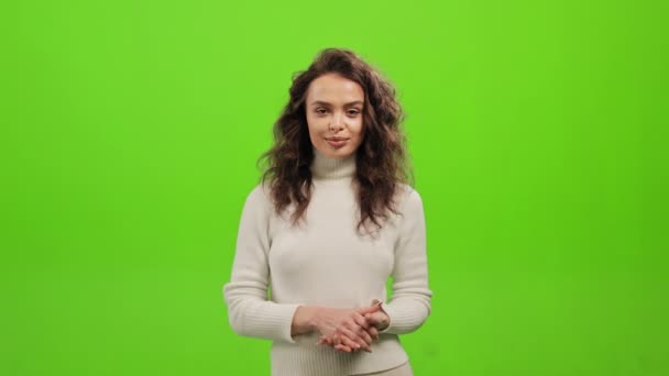 Žena stojí a dívá se do kamery. Drží ruce u sebe a usmívá se. Stojí na zeleném pozadí. Zelená obrazovka. 4K — Stock video