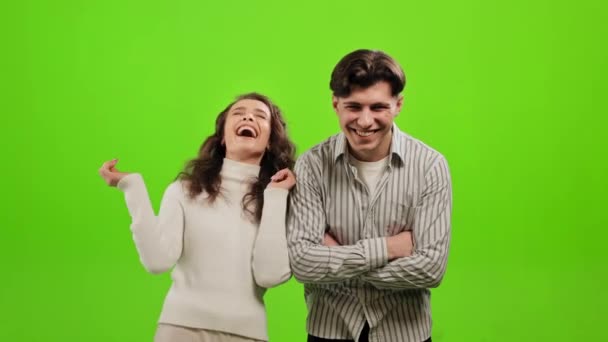 Ένας άντρας και μια γυναίκα στέκονται και κοιτάζουν την κάμερα. Γελάνε πολύ. Στέκονται σε ένα πράσινο φόντο. Πράσινη οθόνη. 4K — Αρχείο Βίντεο