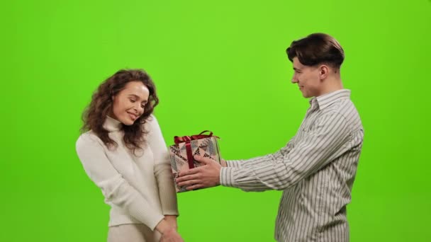 Ένας άντρας δίνει ένα δώρο σε μια γυναίκα. Είναι πολύ χαρούμενη και χαμογελάει. Αγκαλιάζονται. Στέκονται σε ένα πράσινο φόντο. Πράσινη οθόνη. 4K — Αρχείο Βίντεο