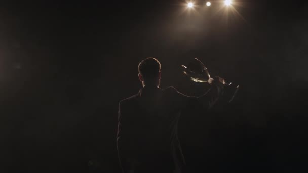 The man is raising the winners goblet. Hes standing on the stage and looking into the audience. Hes wearing a suit and a spotlight is shining on him. 4K — Stock Video