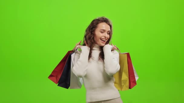 Žena se dívá do kamery a usmívá se. Ona zvedá nákupní tašky. Je velmi šťastná. Stojí na zeleném pozadí. Zelená obrazovka. 4K — Stock video
