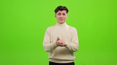 Adam ayakta duruyor ve kameraya bakıyor. O, ellerini çırpıyor. O, yeşil bir arka planın üzerinde duruyor. Yeşil ekran. 4K