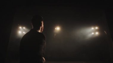 Adam sahneye geliyor ve mikrofonu kaldırıyor. Takım elbise giyiyor. Spot ışıkları onun üzerinde parlıyor. 4K