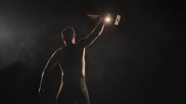 Tayt giymiş bir adam sahnede dikiliyor. Kazananlar kupasını kaldırıyor ve sallıyor. Spot ışıkları onun üzerinde parlıyor. 4K