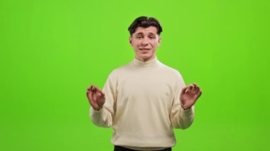 Adam ayakta duruyor ve kameraya bakıyor. Konuşuyor ve ellerini sallıyor. Duygusal ve gülümsüyor. Kameraya konuşuyorum. O, yeşil bir arka planın üzerinde duruyor. Yeşil ekran. 4K