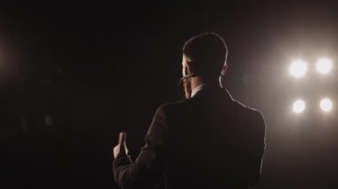 Konferansı konuşmacı yönetiyor. Mikrofona konuşuyor ve ellerini sallıyor. Spot ışıkları onun üzerinde parlıyor. Kamera onun etrafında dönüyordu. 4K