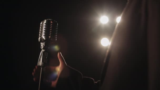 El cantante está tomando un micrófono retro con su mano. El centro de atención está brillando sobre él. Lleva un traje. Disparos de cerca. 4K — Vídeos de Stock