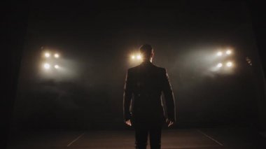 Sahneye bir adam geliyor ve ellerini kaldırıyor. Takım elbise giyiyor ve spot ışıkları onun üzerinde parlıyor. Konuşmacı sahnede sahne alıyor. 4K