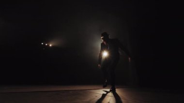 Bir adam duygusal olarak dans ediyor. Spot ışıkları onun üzerinde parlıyor. Takım elbise ve şapka giyiyor. Etrafında duman var. 4K