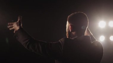 Bir adam sahnede duygusal bir performans sergiliyor. O, ellerini sallıyor ve konuşuyor. Spot ışıkları onun üzerinde parlıyor. Kamera onun etrafında dönüyordu. 4K