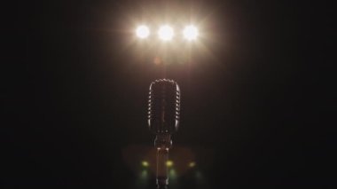 Adam mikrofona yaklaşıyor. Sahnede bir retro mikrofon var. Şarkıcı mikrofona gidiyor. Spot ışıkları onun üzerinde parlıyor. 4K