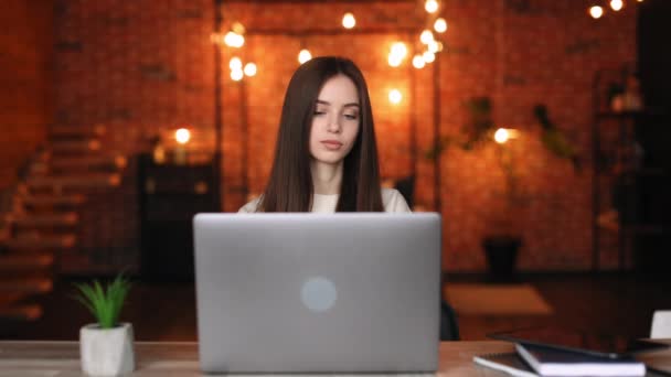 Bir kadın masada oturuyor ve bir dizüstü bilgisayarı kapatıyor. Gülümsüyor ve kameraya bakıyor. Ev ofisinde çalışıyorum. 4K — Stok video