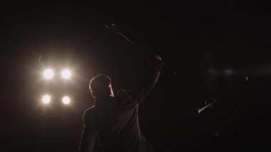 Şarkıcı sahnede duruyor ve mikrofonu onun üzerine kaldırıyor. Spot ışıkları onun üzerinde parlıyor. 4K
