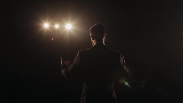 一个男人站在舞台上说话。他挥挥手，谈情说爱。聚光灯照在他身上.演讲者正在舞台上表演.4K — 图库视频影像