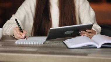 Bir kadın tablet üzerinde çalışıyor. O, defterine notlar alıyor. Başını kaldırıyor ve kameraya bakıyor. Gülümsüyor ve ofisteki bir masada oturuyor. Portre çekimi. 4K