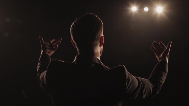 Bir adam sahnede duygusal bir performans sergiliyor. O, ellerini sallıyor ve konuşuyor. Spot ışıkları onun üzerinde parlıyor. 4K — Stok video