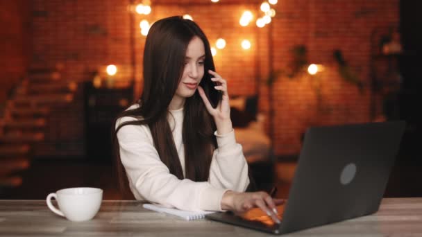 Una donna è seduta nel suo ufficio. Sta lavorando su un portatile e parlando al telefono. 4K — Video Stock