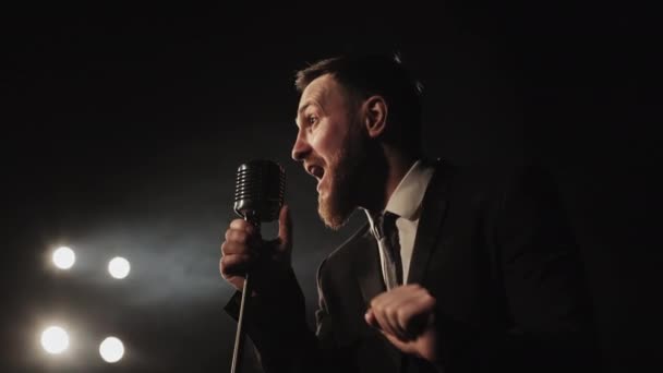 La chanteuse interprète la chanson émotionnellement. Il est debout sur scène et tient le microphone. Il regarde dans le couloir. Les projecteurs brillent sur lui. Tournage de portraits. 4K — Video