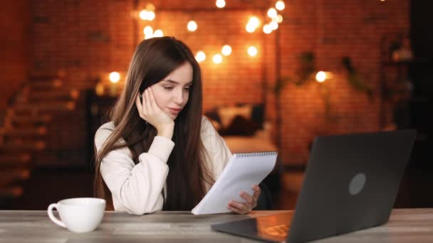 Egy nő ül az otthoni irodájában. A jegyzetfüzetét nézegeti és gondolkodik. 4K — Stock videók