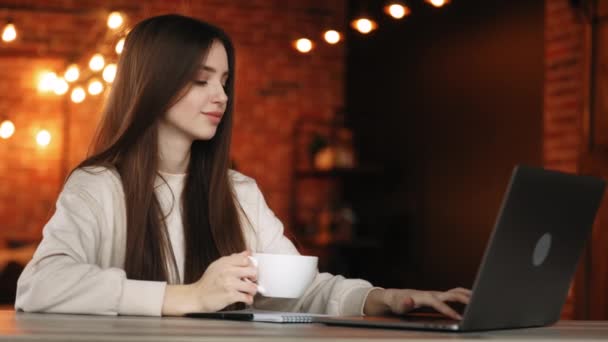 Uma mulher está sentada no seu escritório. Ela está trabalhando em um laptop e segurando uma xícara de chá. 4K — Vídeo de Stock