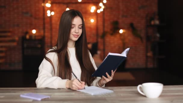 A woman is sitting in her home office. She is reading a book and taking notes in a notebook. She is working. 4K — Stock Video