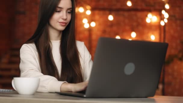 En kvinna sitter på sitt hemkontor. Hon sitter vid sitt skrivbord och jobbar på sin laptop. Det finns en kopp te på bordet. Porträtt fotografering. 4K — Stockvideo