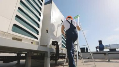 Genç mühendis merdivenleri tırmanıyor ve vidaları anahtarla çeviriyor. Klimayı o çalıştırıyor. Bir iş merkezinin çatısında. Onun yanında bir alet çantası var. O