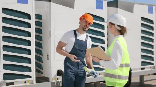 İş bittikten sonra iki mutlu mühendis el sıkışıyor. Bir iş merkezinin çatısında. İş kıyafetleri ve kalın bir şapka giyiyorlar. Güzel güneşli bir gün. 4K — Stok video
