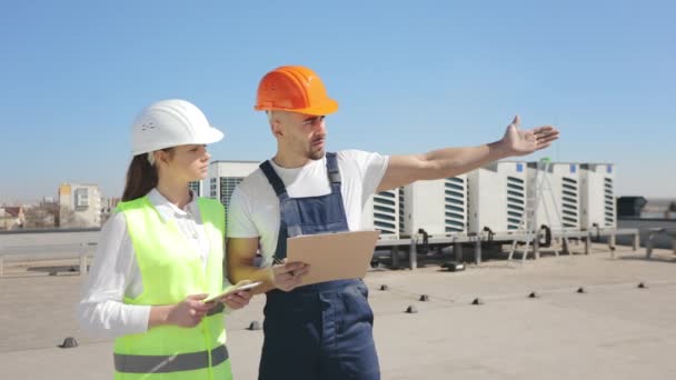 Two engineers are discussing the work done to install the air conditioning system. The engineer is pointing his hand at the object. They are wearing work clothes and a hard hat. Air conditioning — Αρχείο Βίντεο