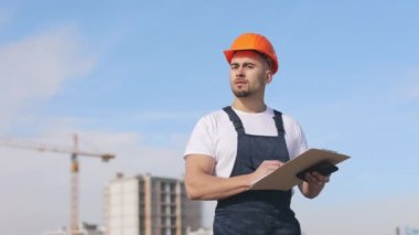 Genç mühendiste bir dosya dolusu belge ve akıllı telefon var. O, kameraya bakıyor. Bir iş merkezinin çatısında. O, iş kıyafetleri ve sert bir şapka giyiyor. Yapım içeri