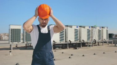 Kafasına koruyucu kask takan bir mühendisin portresi. O mutlu ve kameraya bakıyor. O, iş kıyafetleri giyiyor. Arka planda havalandırma sistemi var. 4K