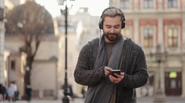 Mutlu sakallı bir adam kulaklıkla müzik dinliyor ve akıllı telefonuyla sosyal ağlarda geziniyor. Gülümsüyor ve eski kasabanın merkezine doğru gidiyor. 4K