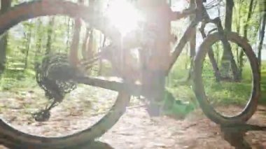 Bir bisikletçi orman yolunda MTB bisikleti sürüyor. O, tepede zıplıyor. Bisikletçilerin ayak pedallarına yakın çekim. Güneş kameraya doğru parlıyor. 4K