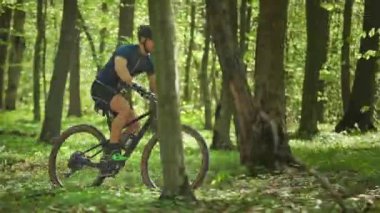 Bisikletli bir adam orman yolundan hızlı geçer. O, hızlı bir koşu yapıyor. Kamera soldan sağa hareket ediyor ve onu takip ediyor. 4K