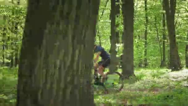 Der Radfahrer rast mit hoher Geschwindigkeit durch den Wald. Er weicht Hindernissen auf dem Weg aus. Die Kamera folgt ihm parallel. Im Vordergrund stehen Bäume. 4K — Stockvideo