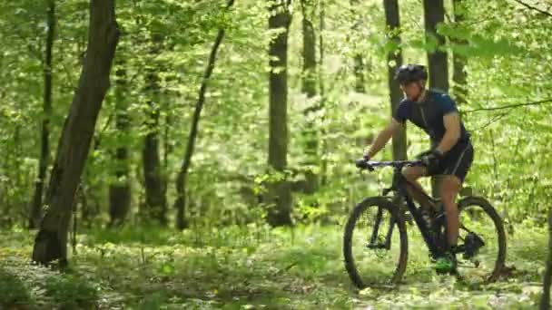 Rowerzysta szybko przechodzi przez leśną drogę. Robi szybki sprint. Jedzie wokół upadłych drzew. Kamera porusza się od prawej do lewej i podąża za nim. 4K — Wideo stockowe