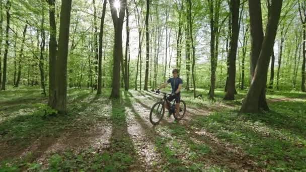 Un hombre está parado en una bicicleta en el bosque. Está mirando a la cámara. Entrenamiento en una bicicleta MTB. La cámara lo atropella. 4K — Vídeos de Stock