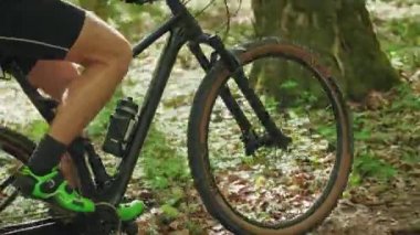 Bir bisikletçi bisiklete biniyor. Kamera onu pedal çevirirken ve hareket ederken çekiyor. Güneş ağaçların arasından parlıyor. 4K