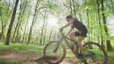 Bir bisikletçi ormanda yüksek hızda gidiyor. Kamera ona paralel hareket ediyor. Bisiklet kıyafeti giyiyor. Güneş ağaçların arasından parlıyor. 4K 50fps