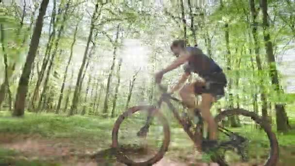 Un ciclista sta pedalando ad alta velocità attraverso la foresta. La telecamera si muove parallela a lui. Indossa l'attrezzatura da ciclismo. Il sole splende tra gli alberi. 4K 50fps — Video Stock