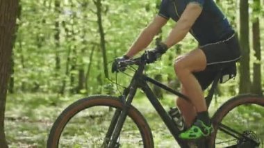 Bir bisikletçi orman yolu boyunca gidiyor. Kamera onun pedal çevirdiği gerçeğine odaklanmış durumda. Sağdan sola doğru gidiyor. 4K