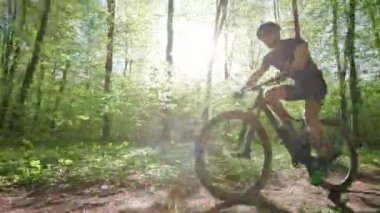 Bir bisikletçi orman yolu boyunca gidiyor. Dönüşümlü çalışıyor. Kamera onun etrafında hareket ediyor. Güneş ağaçların arasından parlıyor. 4K 