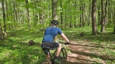 Bisikletli bir adam orman yolunda gidiyor. Kamera onu arkadan takip ediyor. Bisiklet kıyafeti giyiyor. MTB bisikleti üzerinde antrenman. 4K 