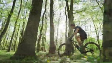 MTB motorlu bir bisikletçi yüksek hızda ormanda ilerliyor. Kamera ona paralel hareket ediyor. Güneş ağaçların arasından parlıyor. Bisiklet kıyafeti giyiyor. 4K 