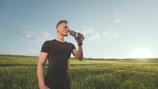 Sportivul stă pe teren și bea apă dintr-o sticlă. Poartă uniformă sportivă. Apus de soare. Fotografiere portret. 4K — Videoclip de stoc