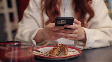 Yarısı yenmiş tatlı ve çatalın üzerinde akıllı telefonu tutan kadınların yakın çekimi. İçeriğe bakmak ya da arkadaşlarla internette sohbet etmek. Tatlı pasta ve içkinin tadını çıkardıktan sonra kafe masasında dinleniyorum..